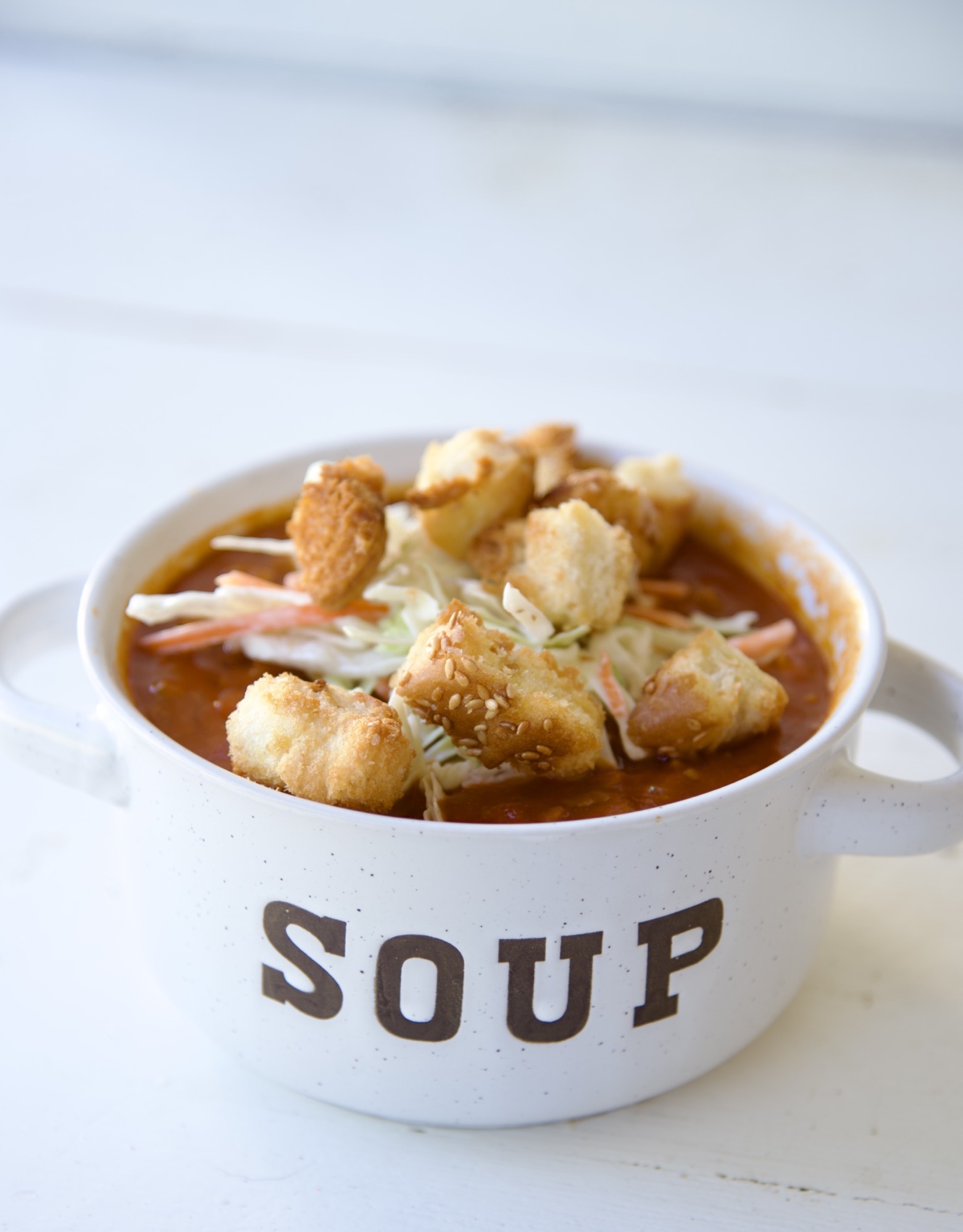 Side view of the soup in a bowl that reads soup and has coleslaw and croutons piled on top.