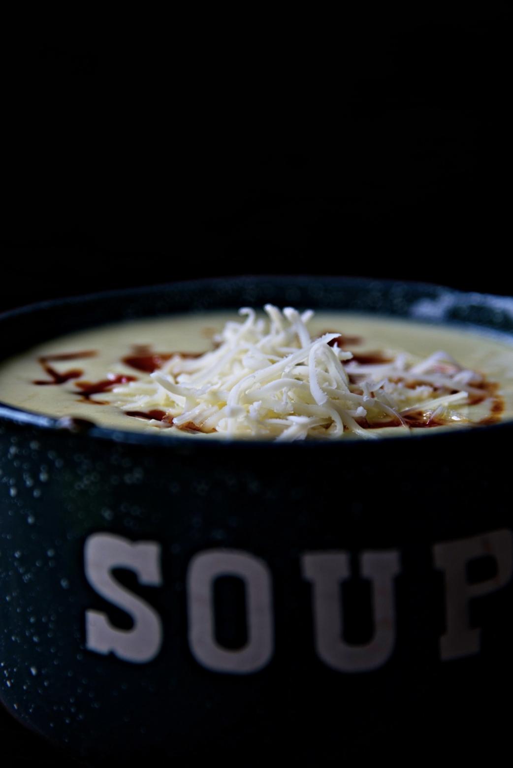 Close up side view of soup with shredded cheese popping up out of the bowl. 