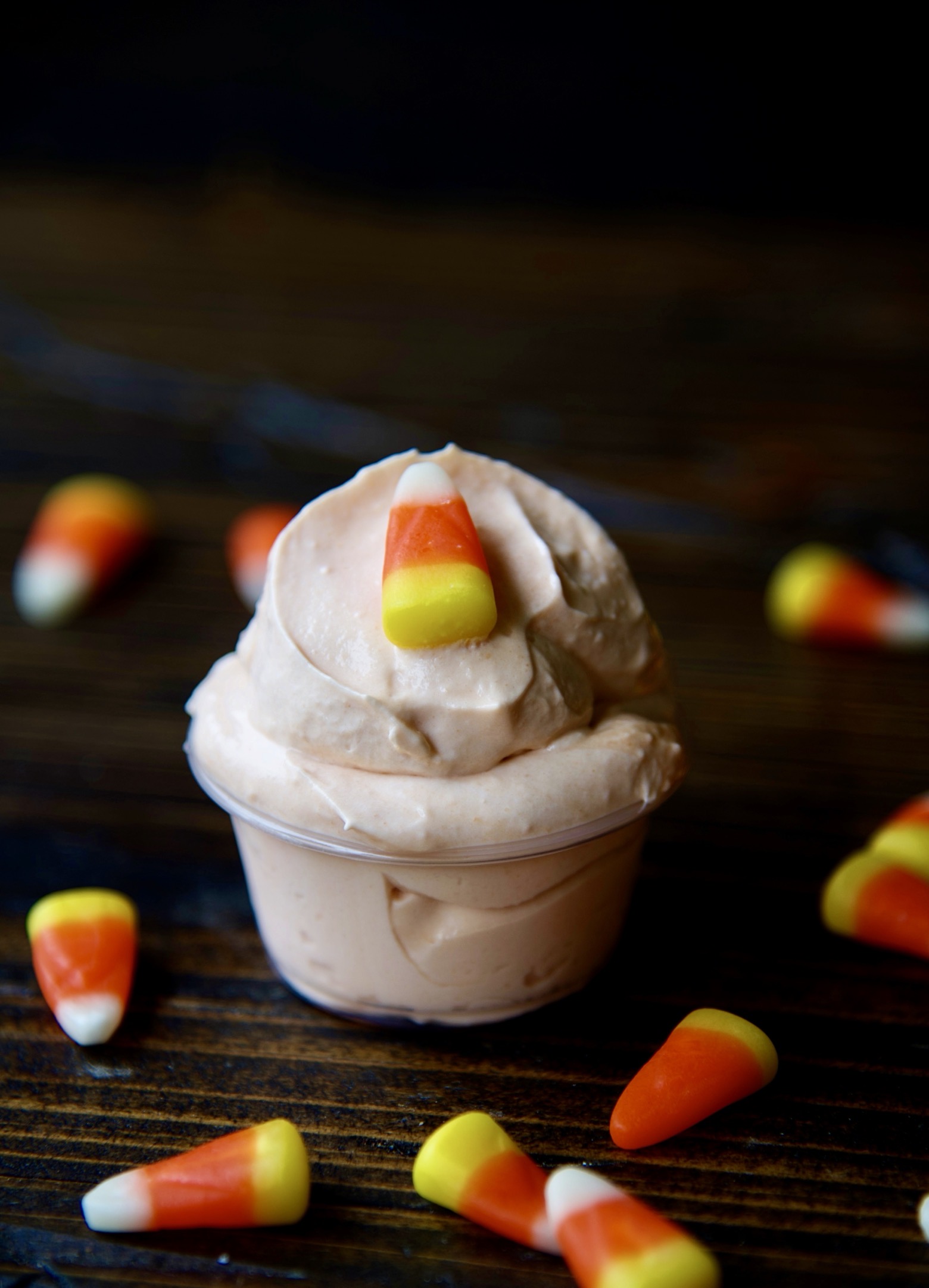Side view of a single pudding shots with candy corn scattered around. 