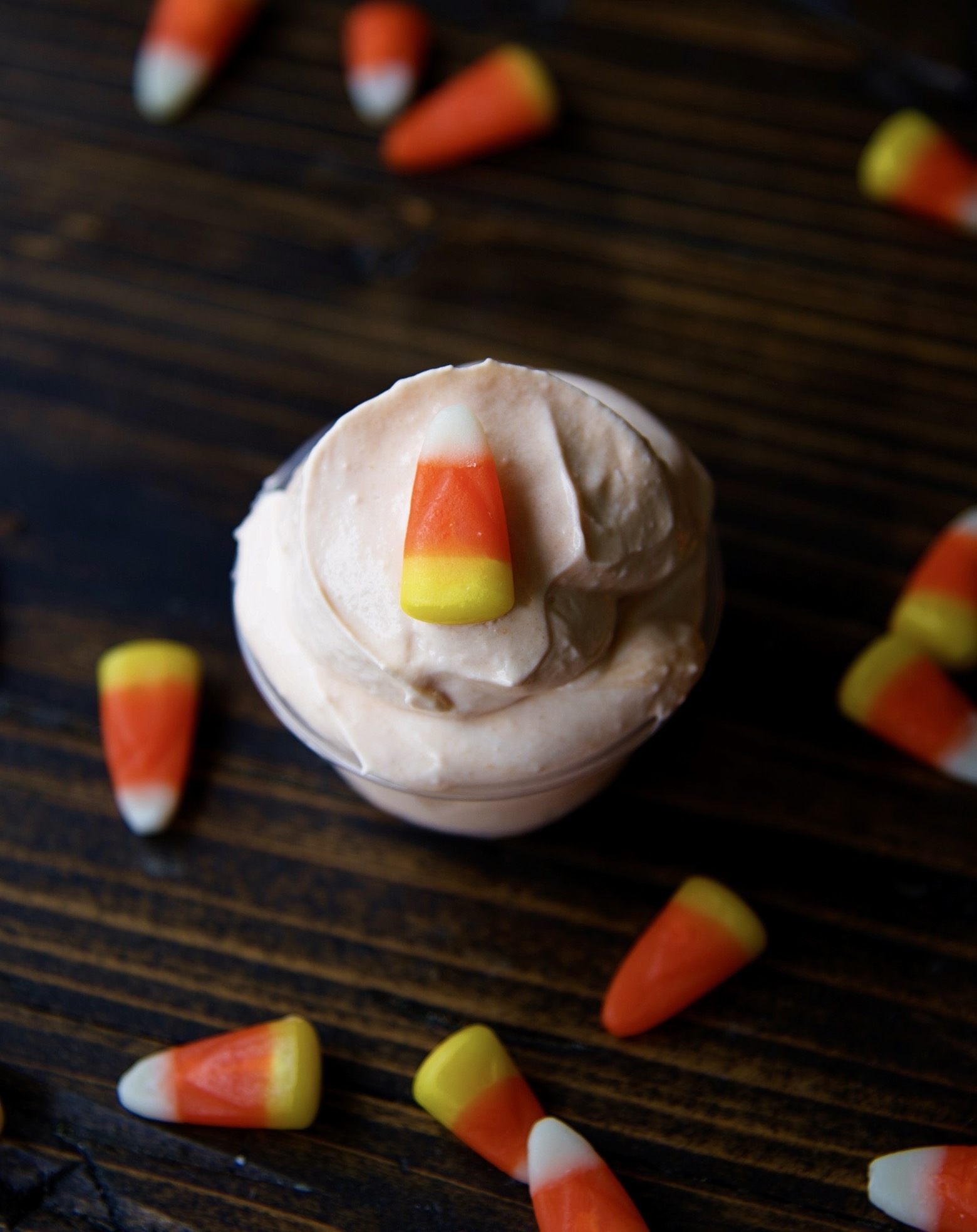 Overhead shot of a single candy corn pudding shot with candy corn around the shot. 