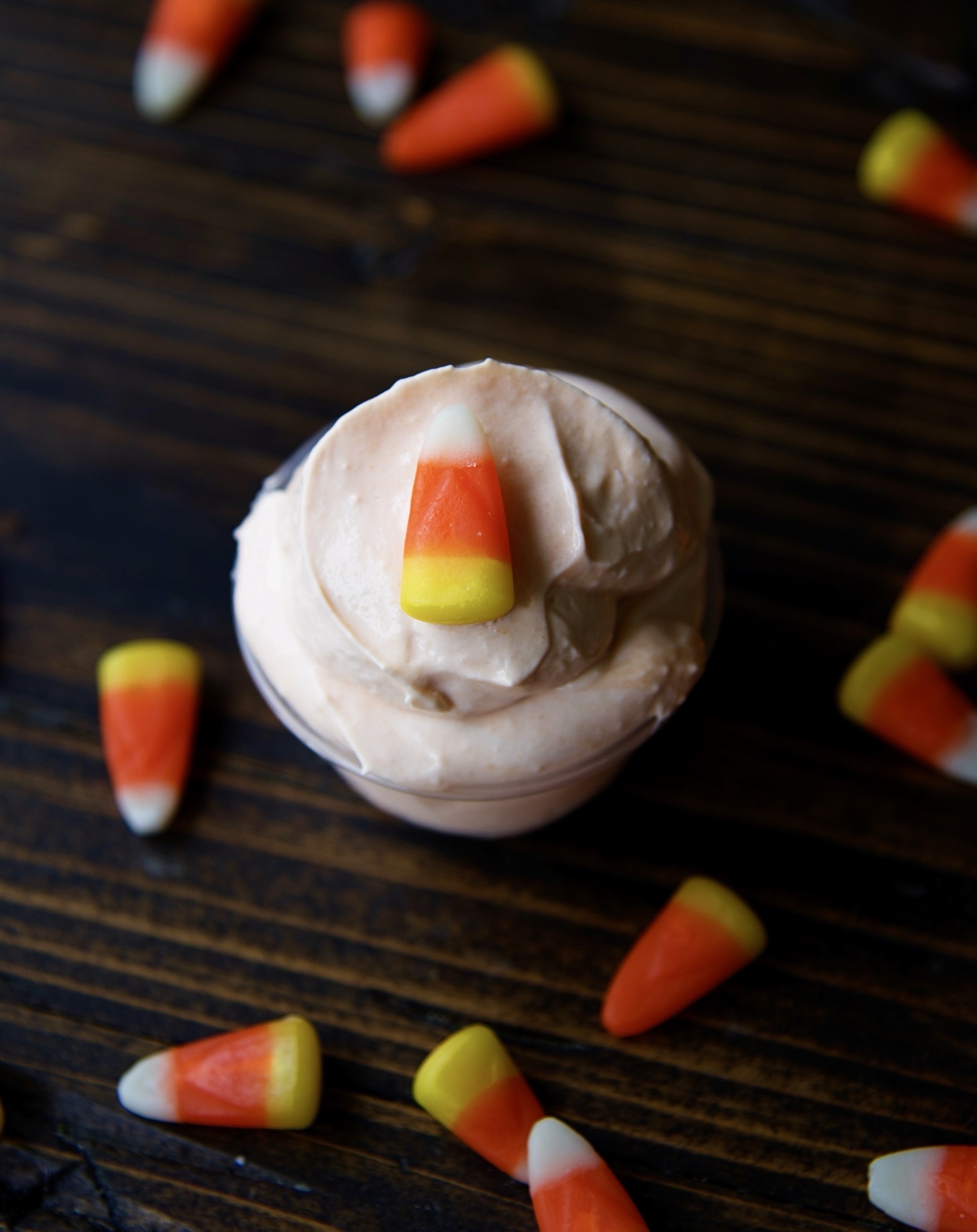 Overhead shot of a single candy corn pudding shot with candy corn around the shot.