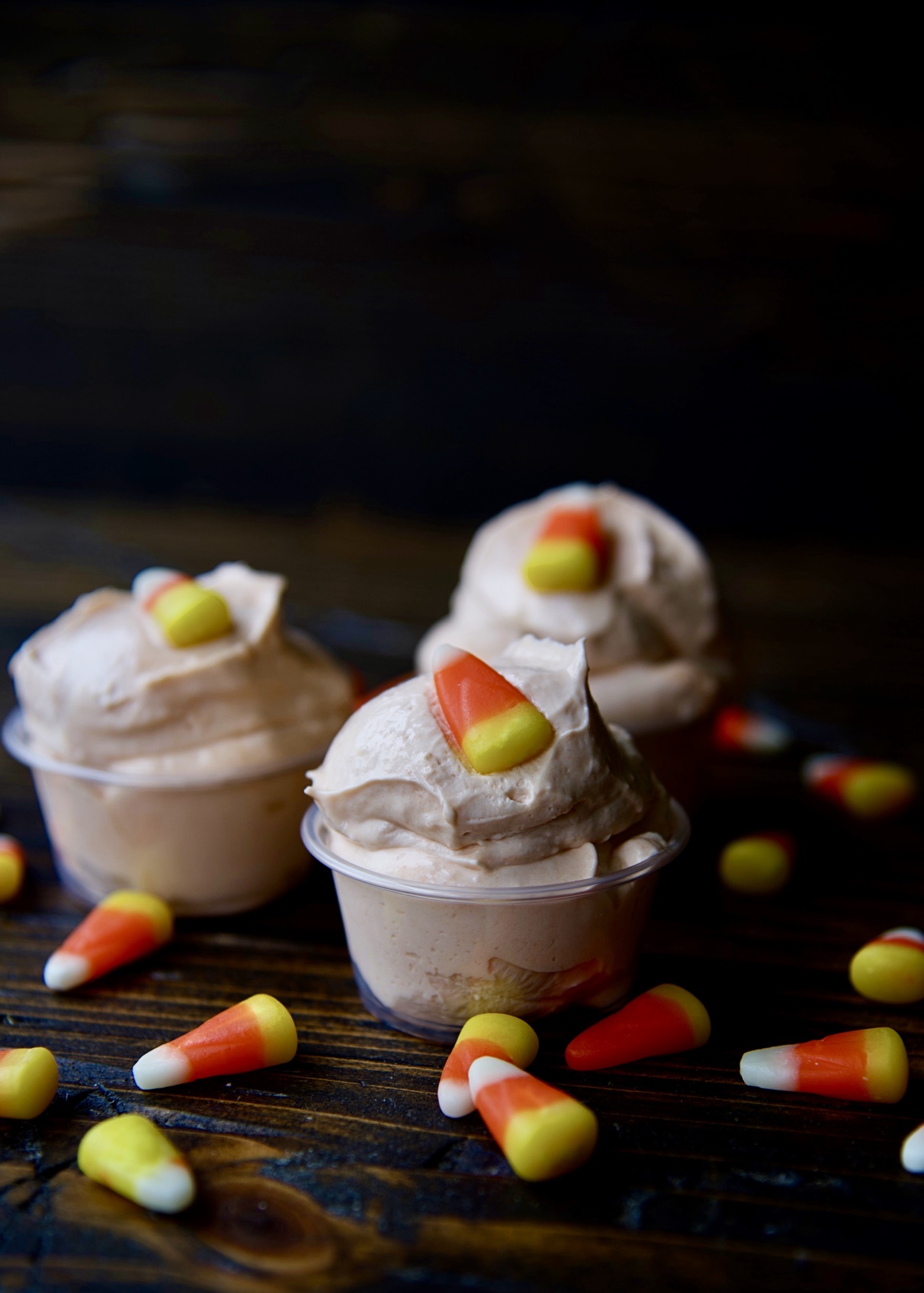 Side view of three pudding shots with candy corn scattered around. 