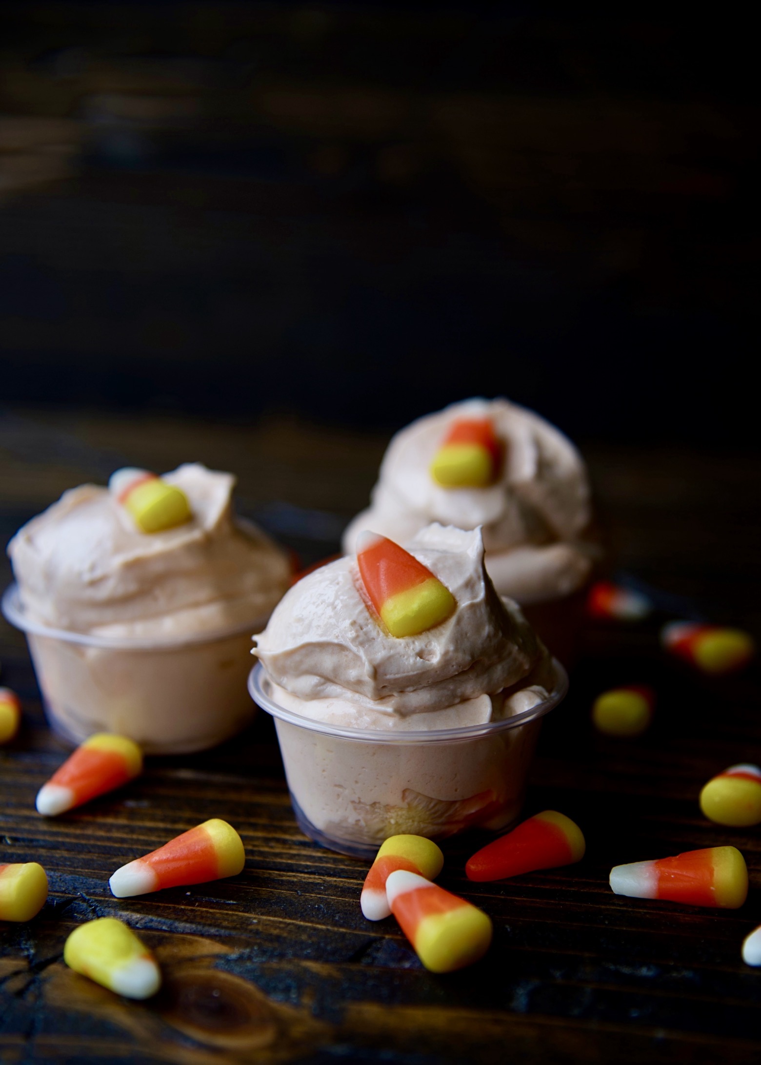 Side view of three pudding shots with candy corn scattered around.