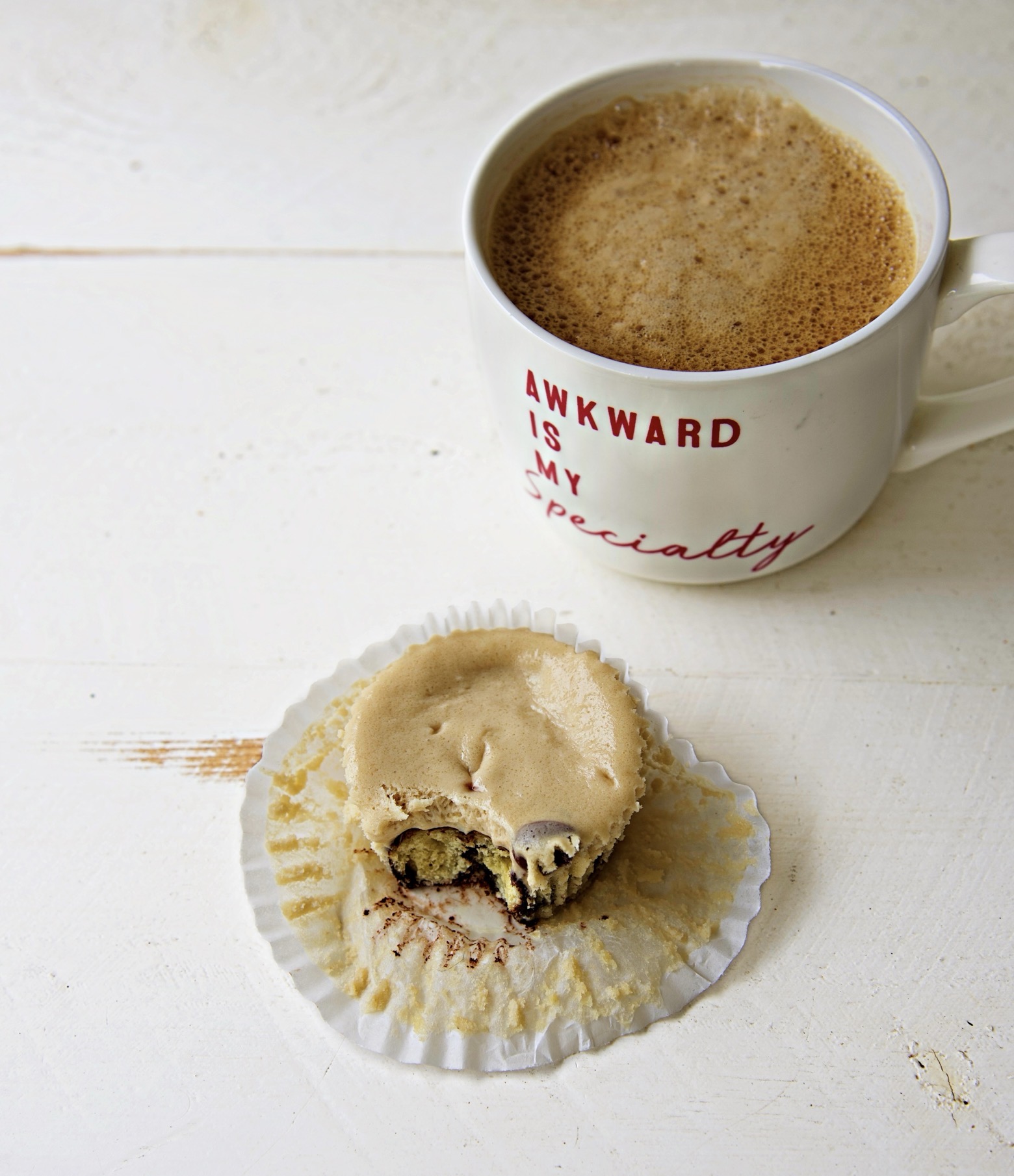 Coffee and Donuts Cheesecake Bite with the cupcake liner pulled back exposing half of the cheesecake bite. With a cup of coffee in the upper right hand corner with a cup that reads Awkward is my specialty. 