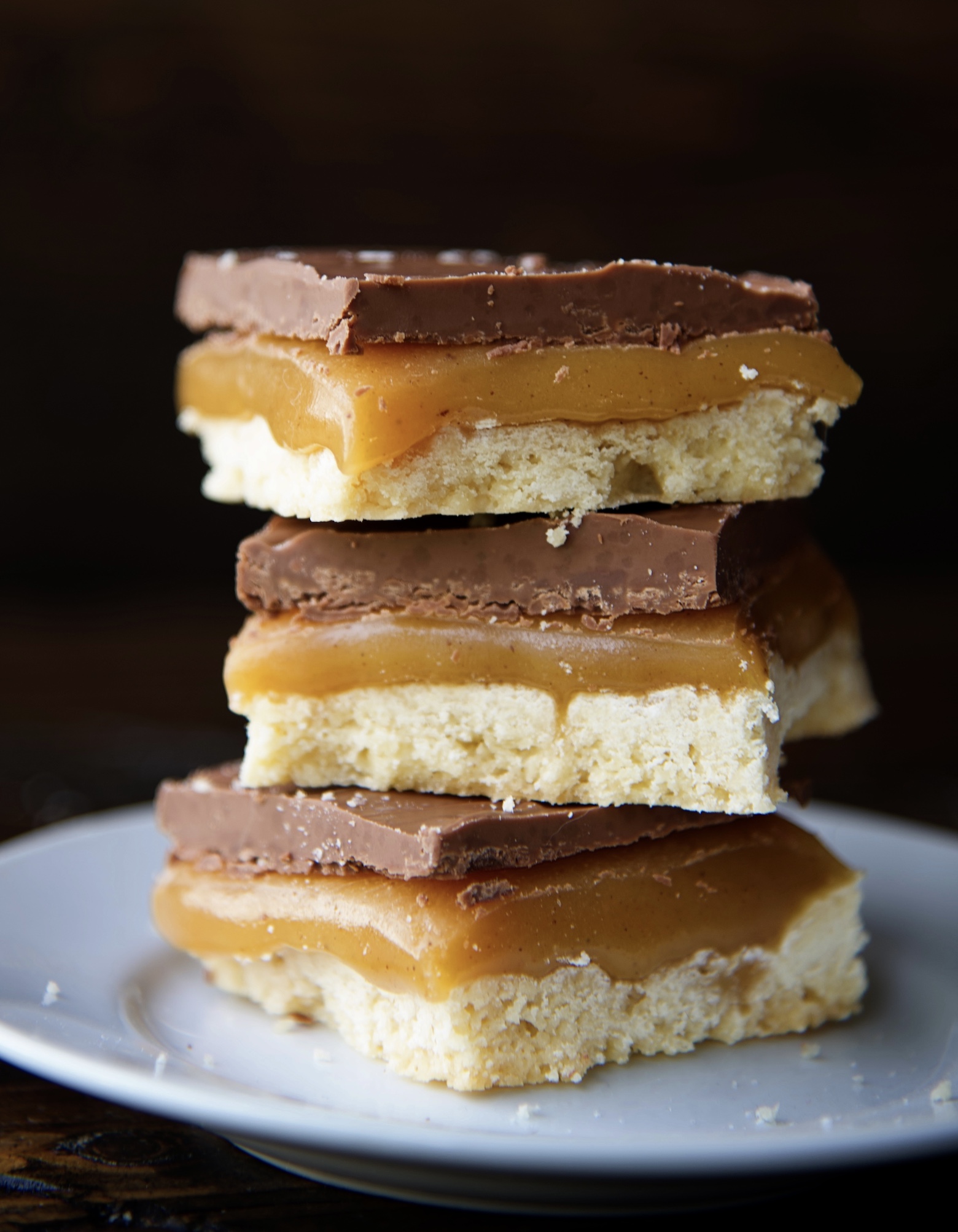 Stack of three millionaire bars on a small white plate. Focus on the caramel in the bars. 