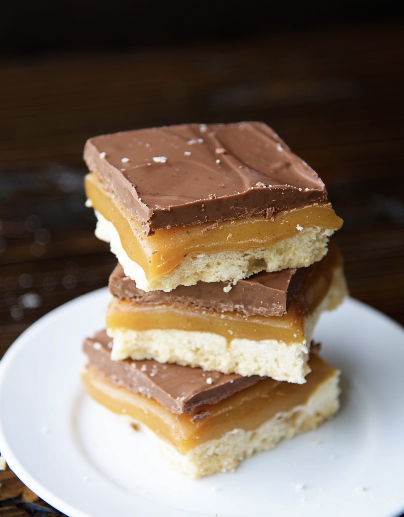 Stack of three millionaire bars on a small white plate. Focus on the caramel in the bars. 