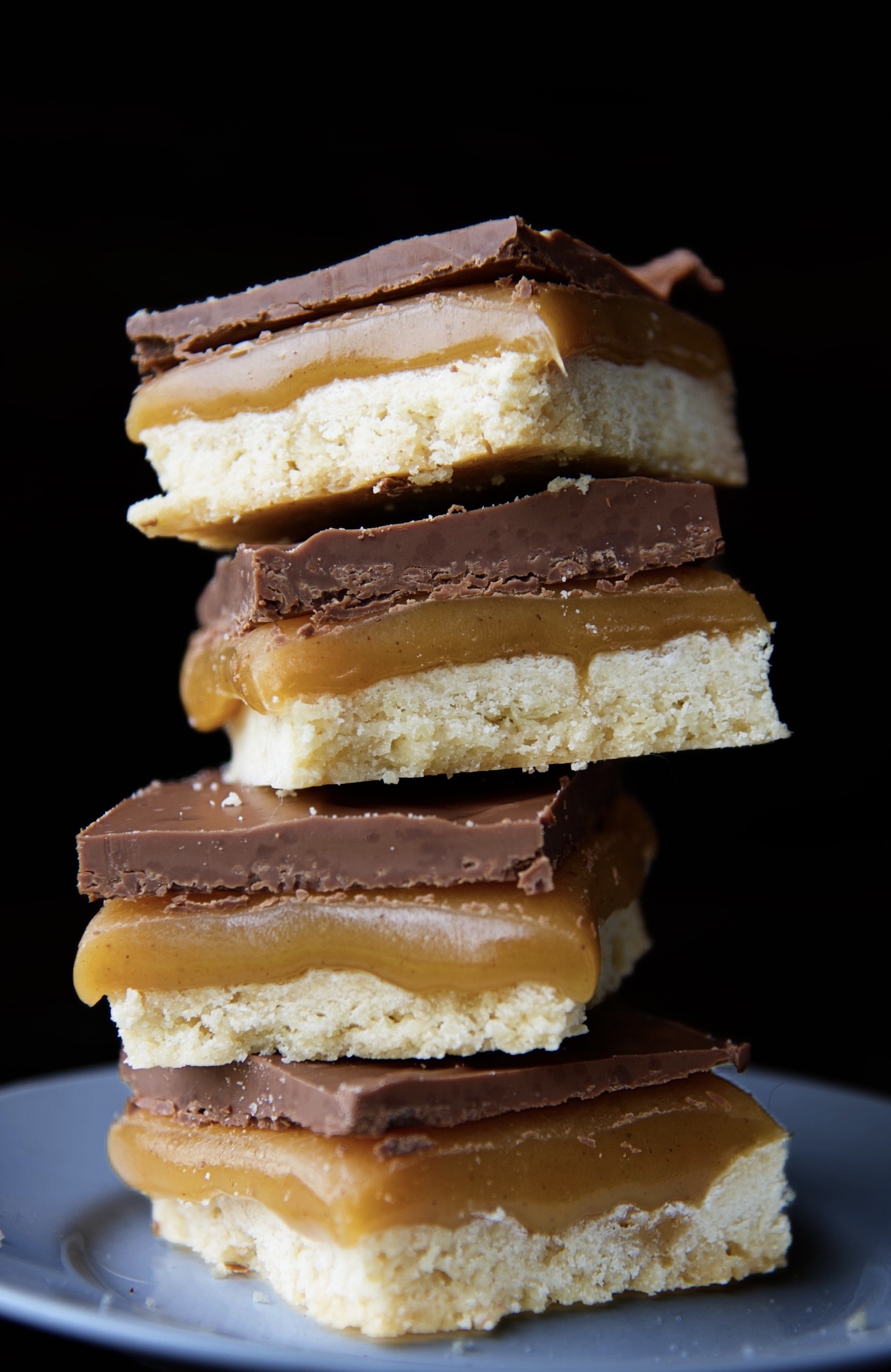 Stack of four millionaire bars on a small white plate. Focus on the caramel in the bars. 