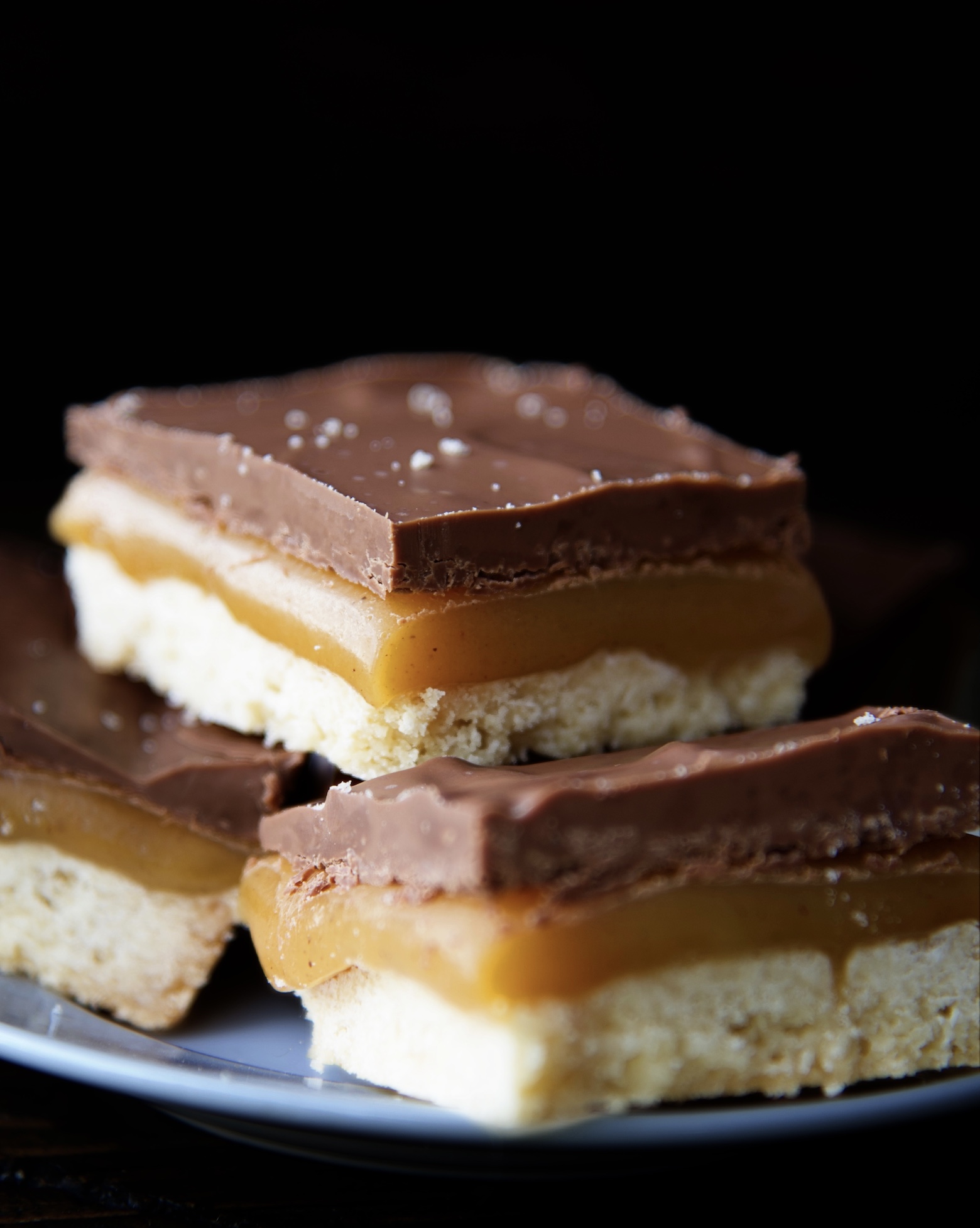 Eggnog Millionaire Shortbread Bar sitting on top of two Eggnog Millionaire Shortbread Bars with the focus on the top bar. 