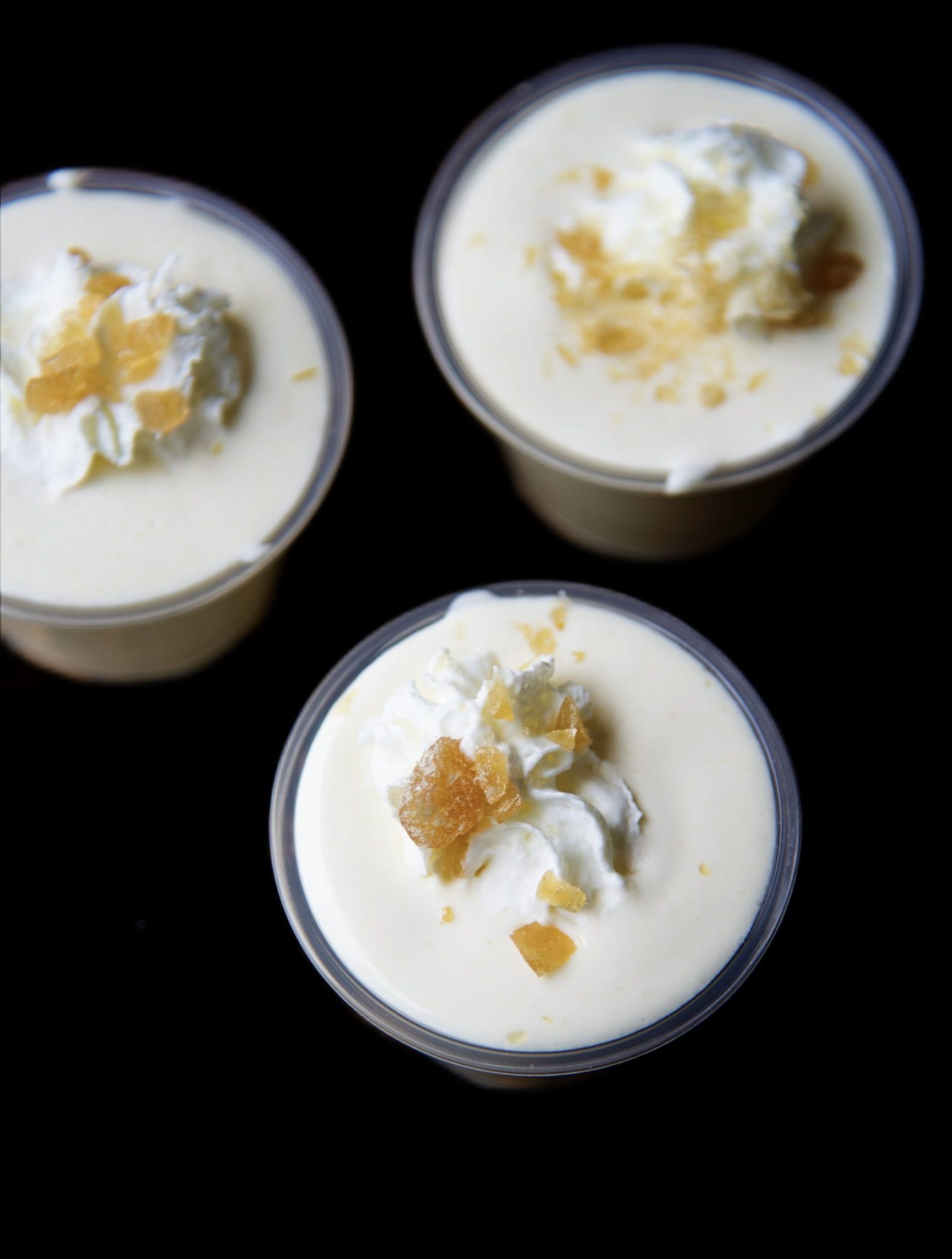 Overhead shot of three pudding shots with the lower one being the focus. Shots are topped with whipped cream and crushed butter rum candies. 
