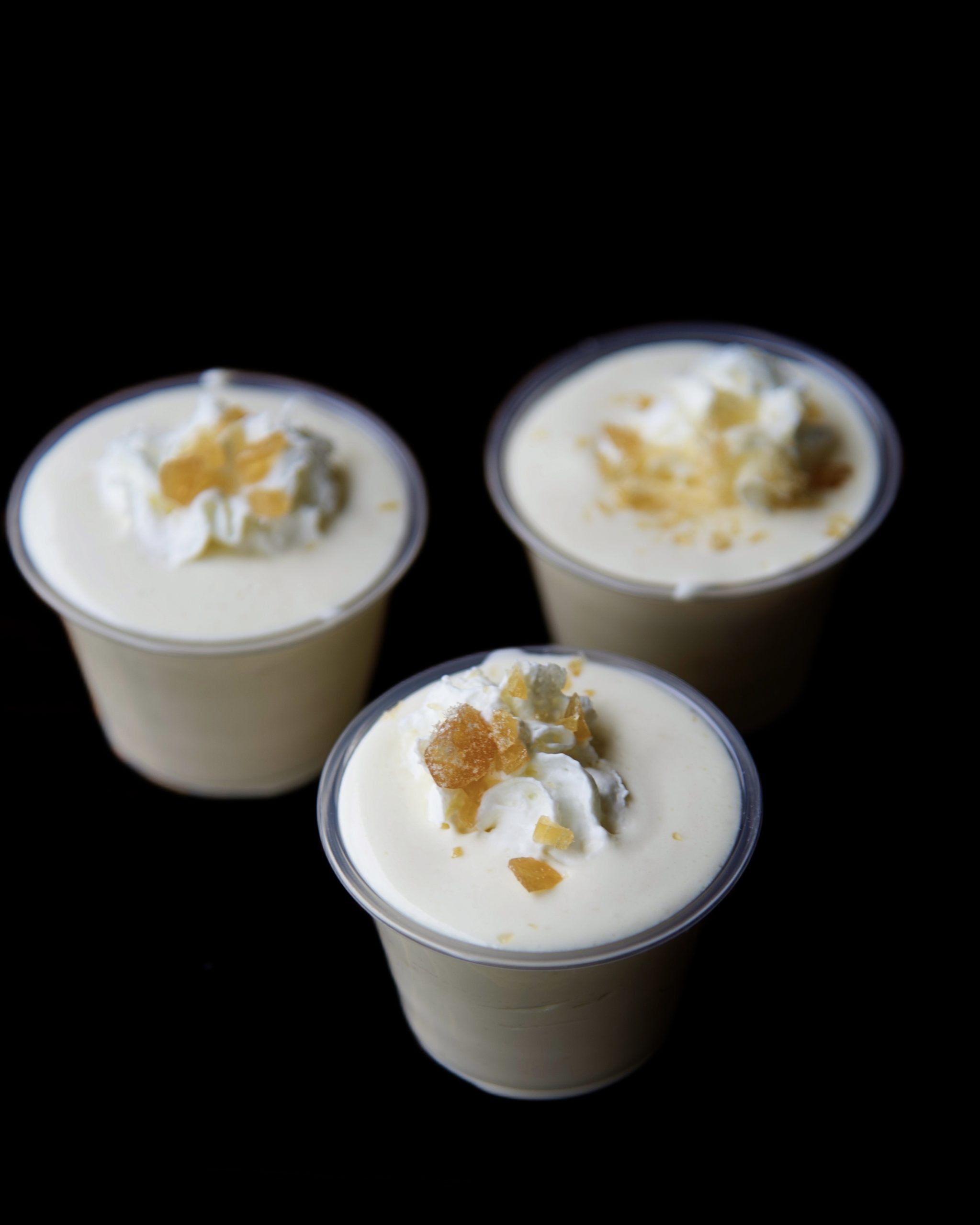 Three pudding shots with the center one being the focus. Shots are topped with whipped cream and crushed butter rum candies. 