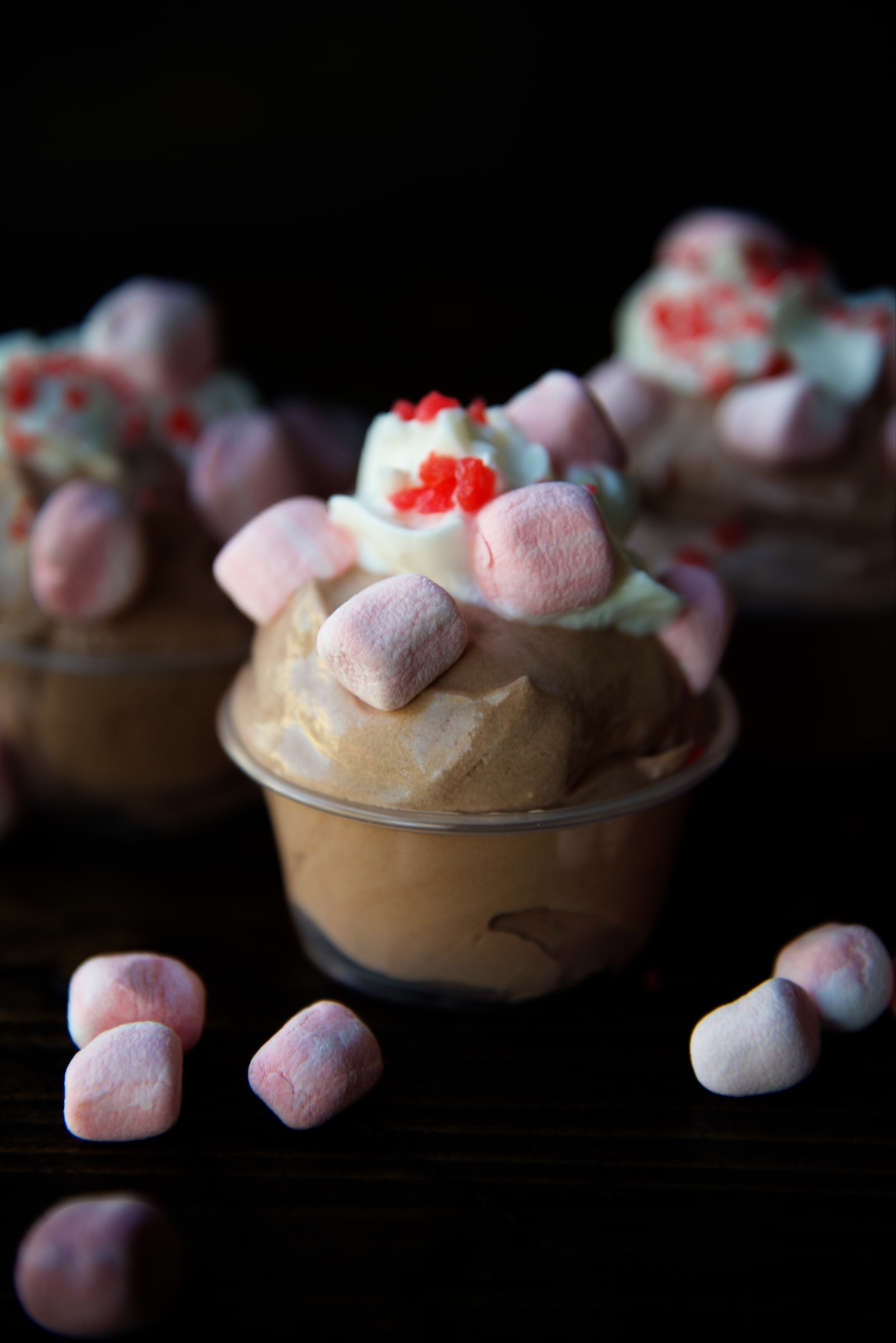 Side view of three pudding shots with peppermint marshmallows scattered around. 