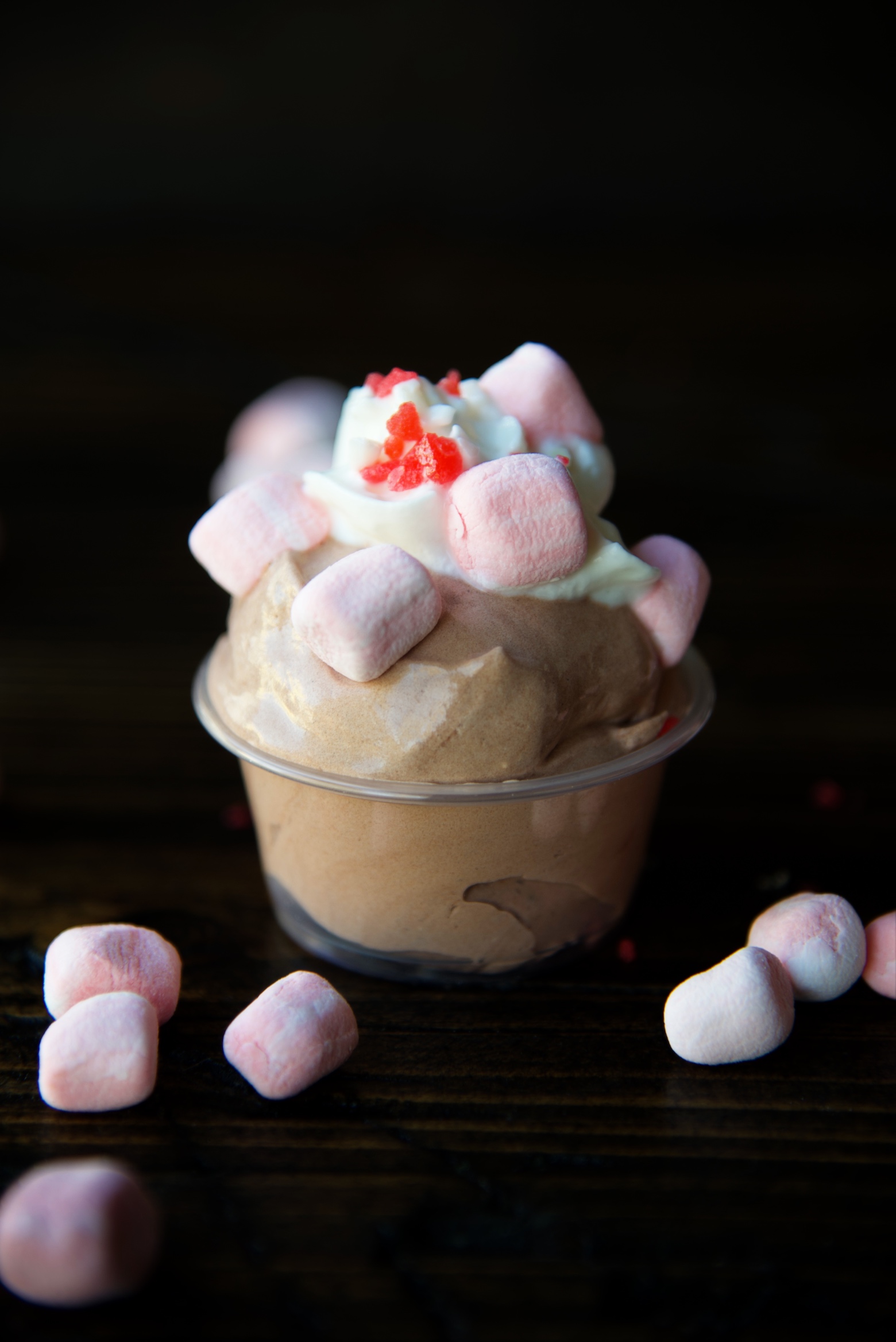 Side view of a single pudding shots with peppermint marshmallows scattered around. 