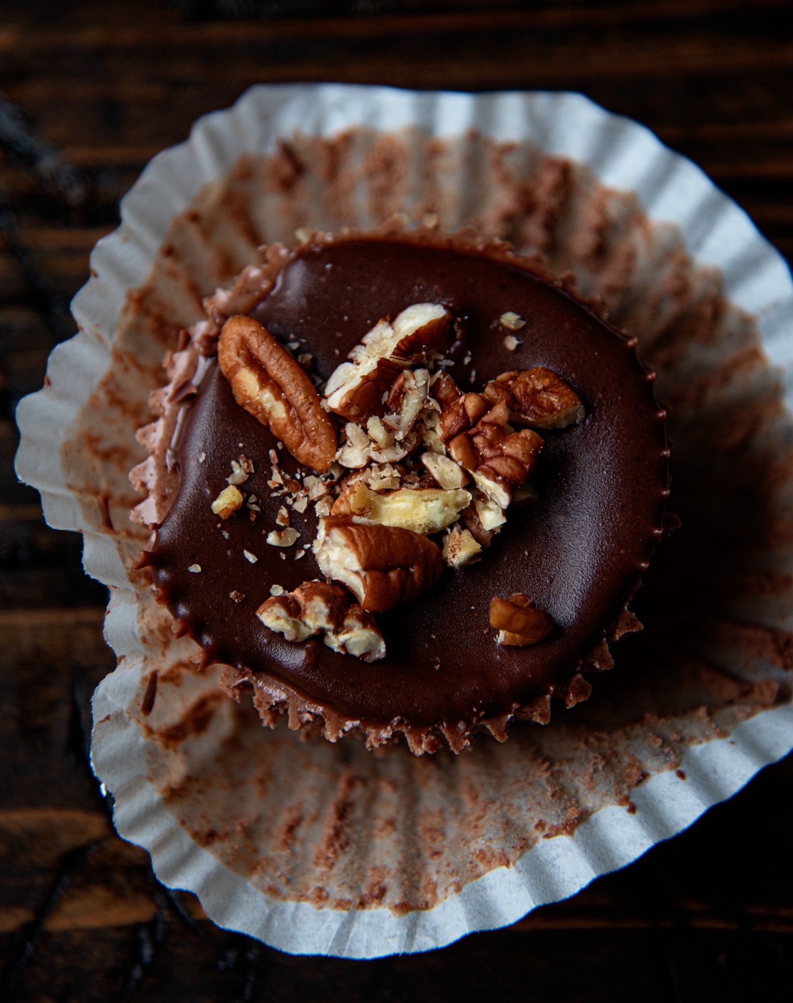 Overhead shot of a cheesecake bite with the focus on the top icing and pecans. The cupcake liner is pulled down. 