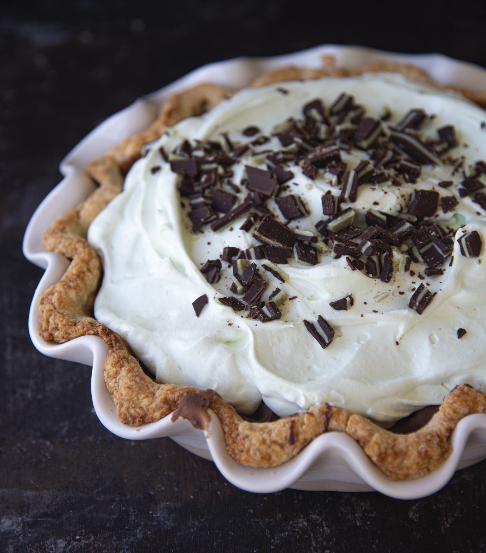 Close up of the crust and top of the pie. The pie has green whipped cream and has pieces of Andes Mints on top. 