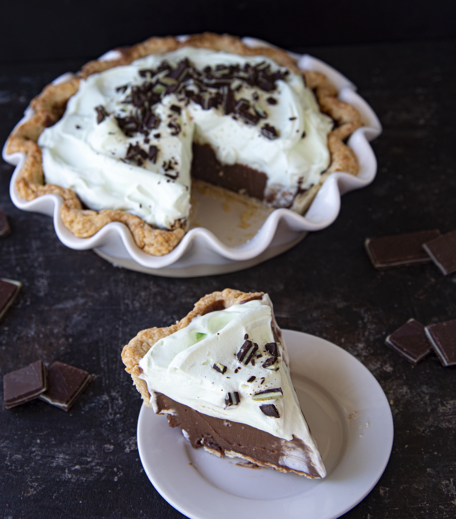 Slice of Andes Mint Chocolate Cream Pie on a small white plate out in front of the whole pie which is in the background. 