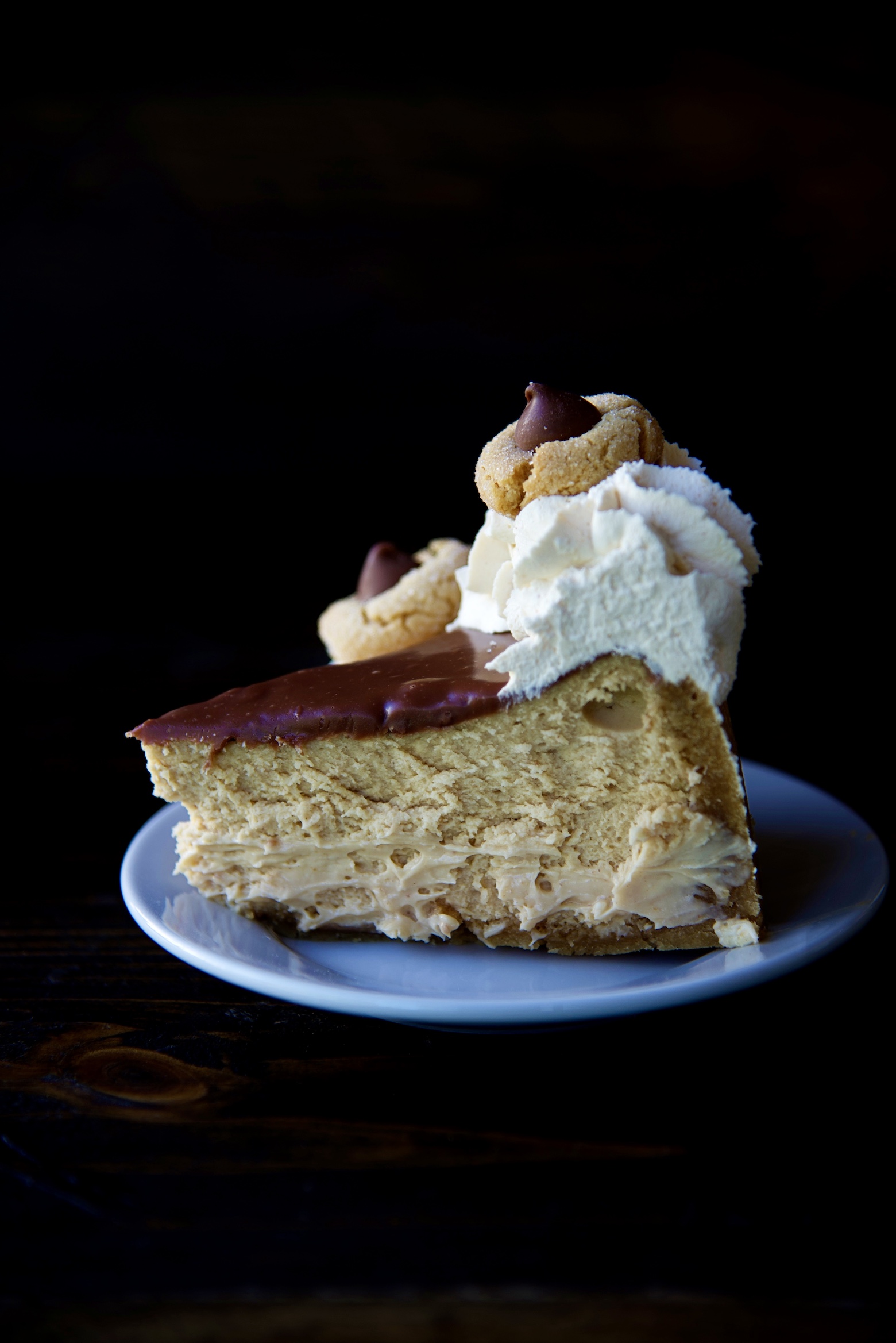 Single slice of cheesecake topped with whipped cream and mini peanut butter blossom cookie