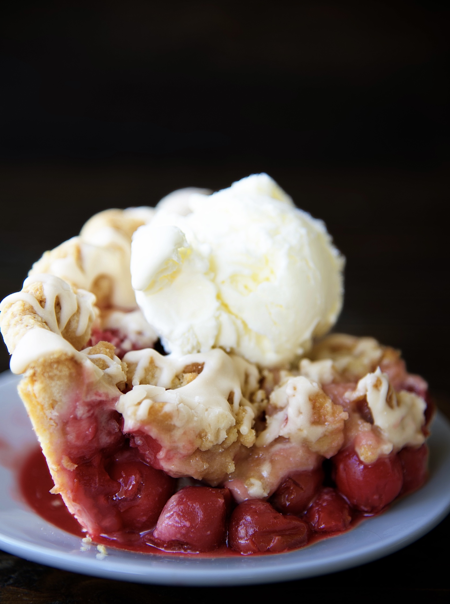 Side view of a slice of Cherry Cola Crumb Pie on a small white plate with vanilla ice cream on top of the slice of pie. 