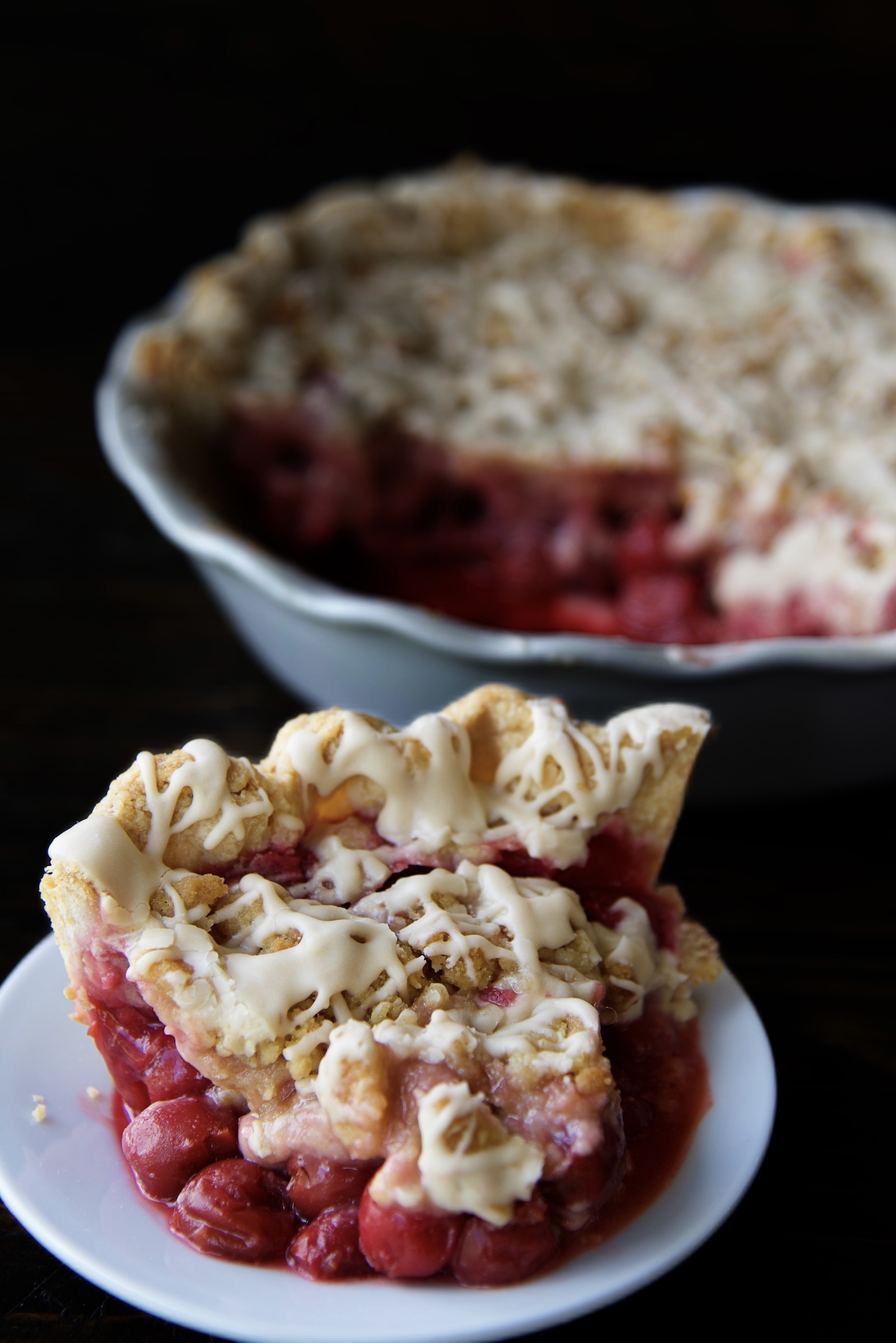 Slice of Cherry Cola Crumb Pie on a small white plate with the remaining pie behind it. 