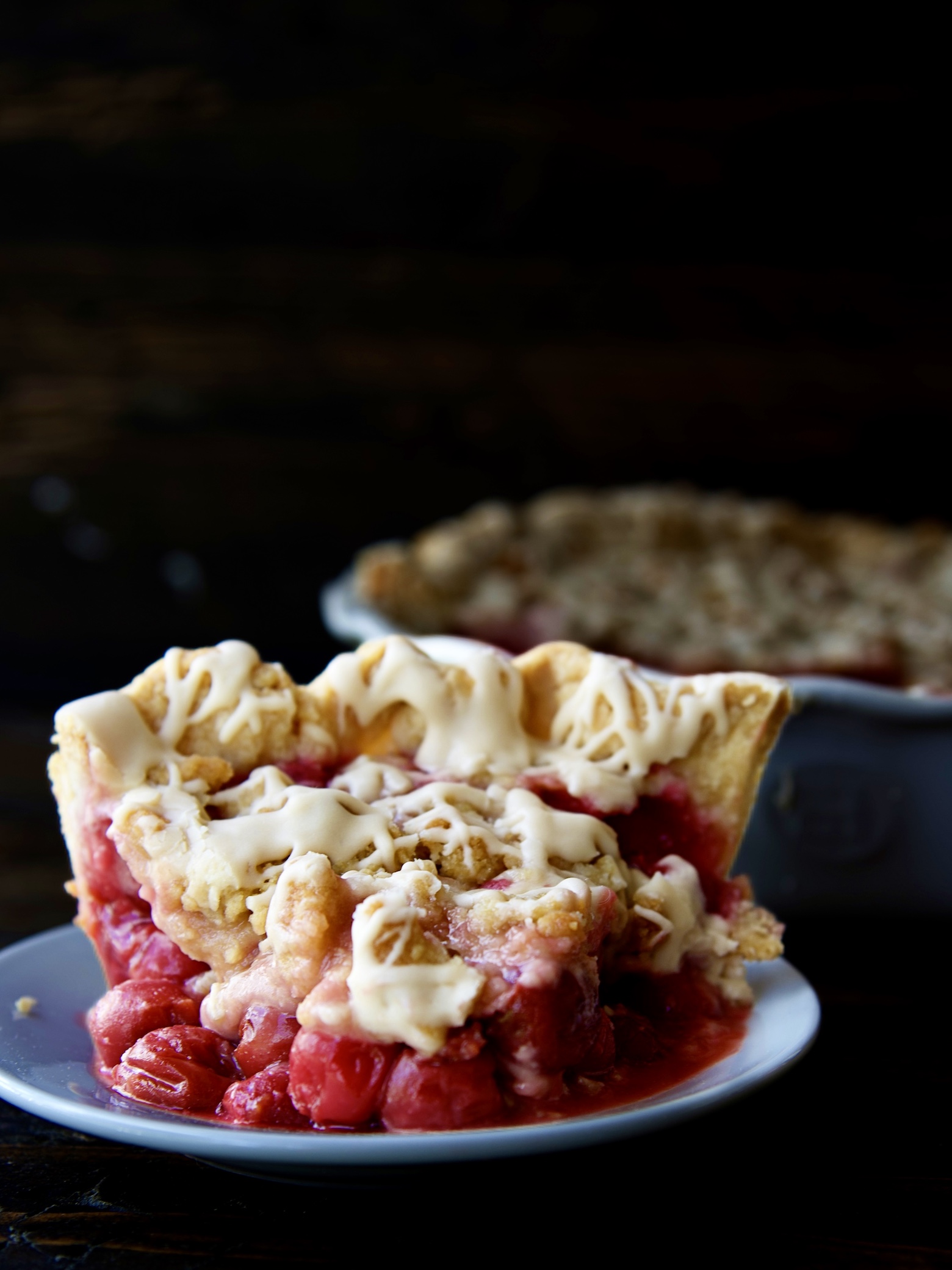 Slice of Cherry Cola Crumb Pie on a small white plate with the remaining pie behind it. 