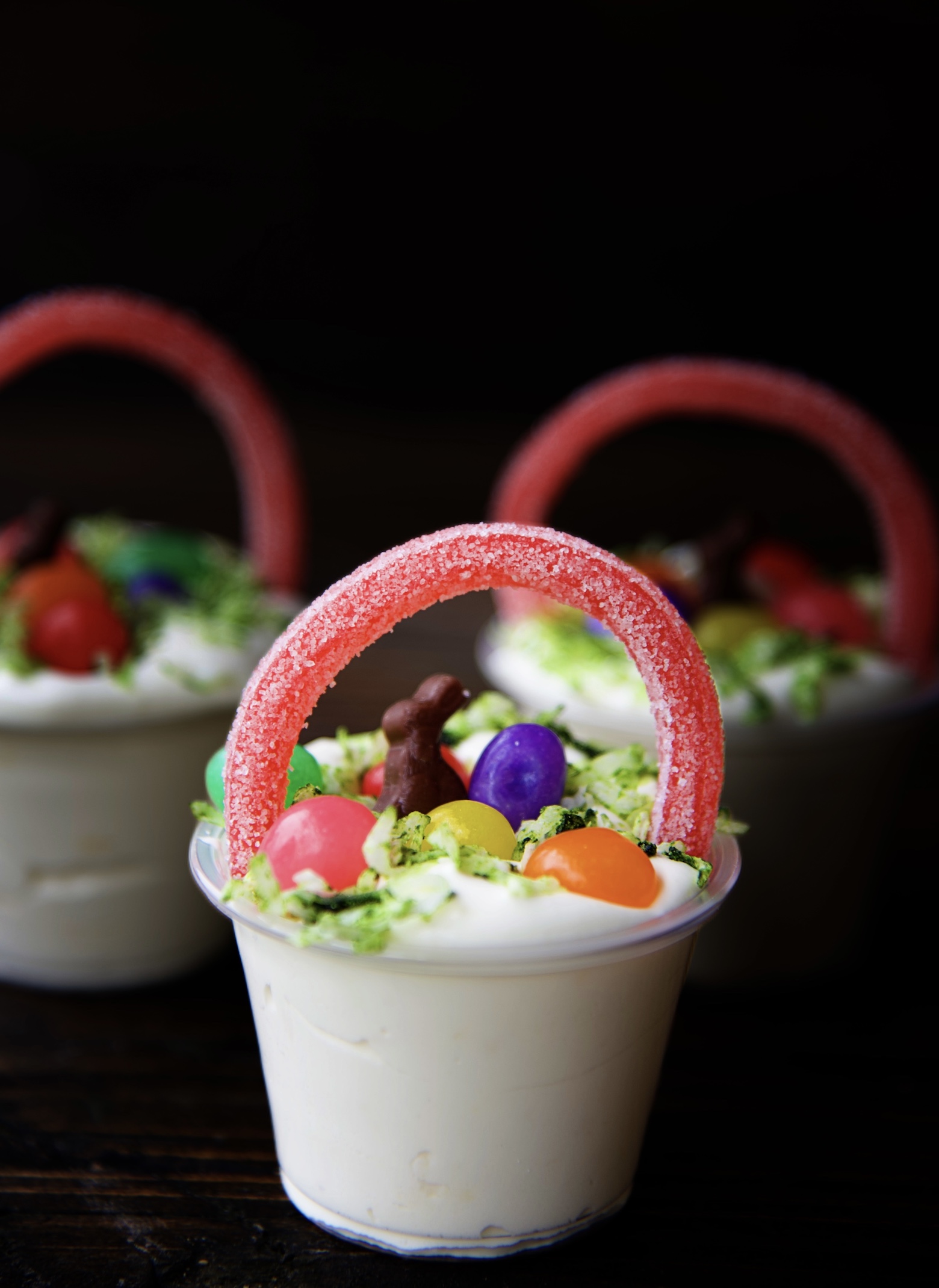 Side view of three pudding shots with with licorice handle, coconut grass, mini chocolate bunny, and mini jelly beans.  