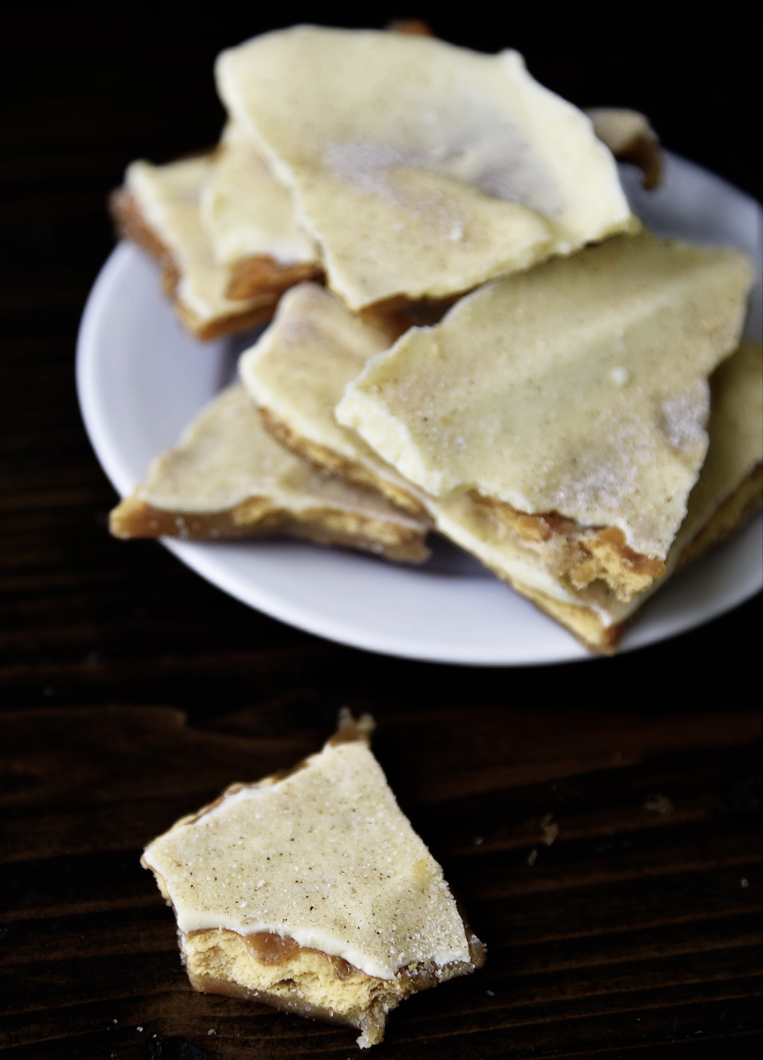 Three quarter view of a single piece of cracker toffee out in front of a small plate of cracker toffee. 