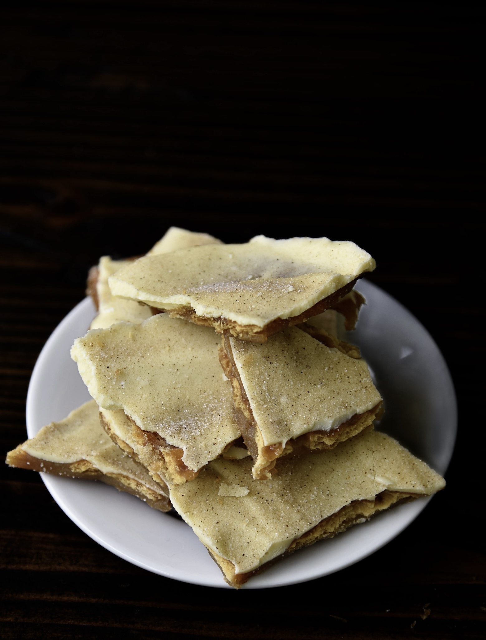 Three quarter view of piece of Cinnamon Churro Cracker Toffee stacked on a small white plate. 