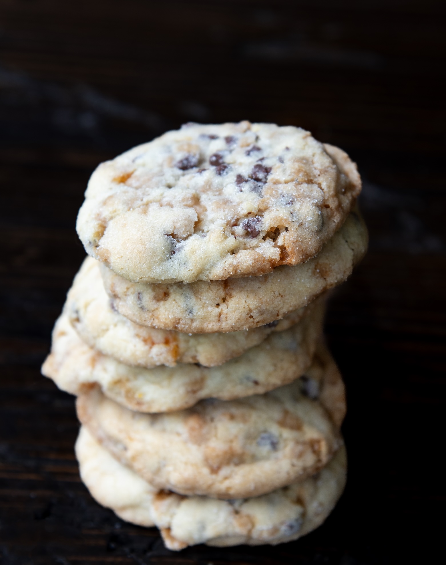 Stack of soft, golden chocolate chip cookies with slightly crisp edges and visible chocolate chips, set against a dark wooden background.