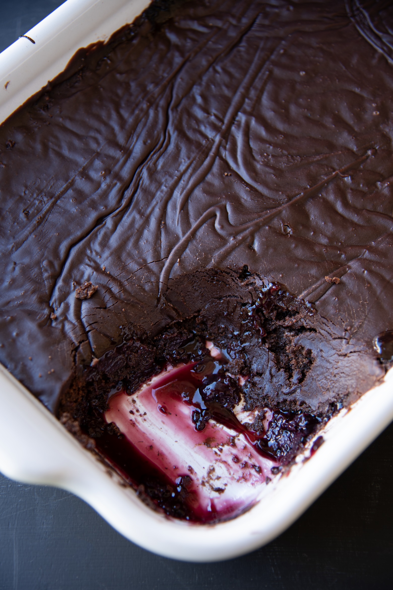 Chocolate blackberry dump cake in a white baking dish with a slice removed, revealing gooey blackberry filling beneath a smooth, fudgy chocolate top.