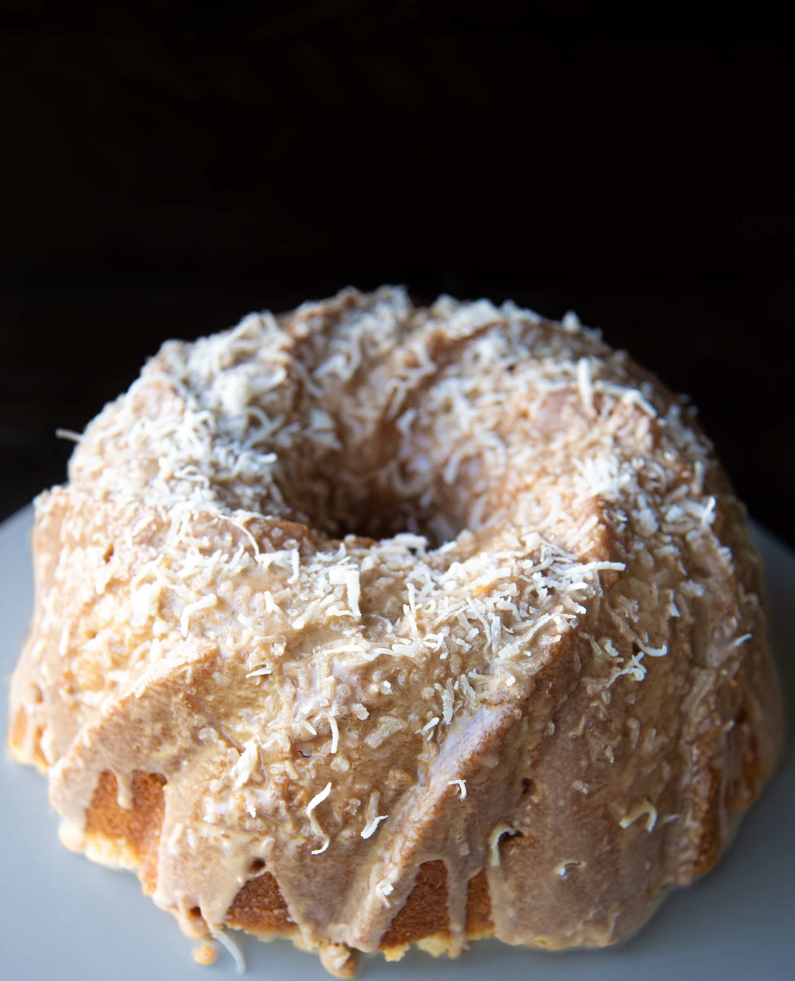 Pineapple coconut Bundt cake topped with creamy coconut frosting and shredded coconut on a white plate.