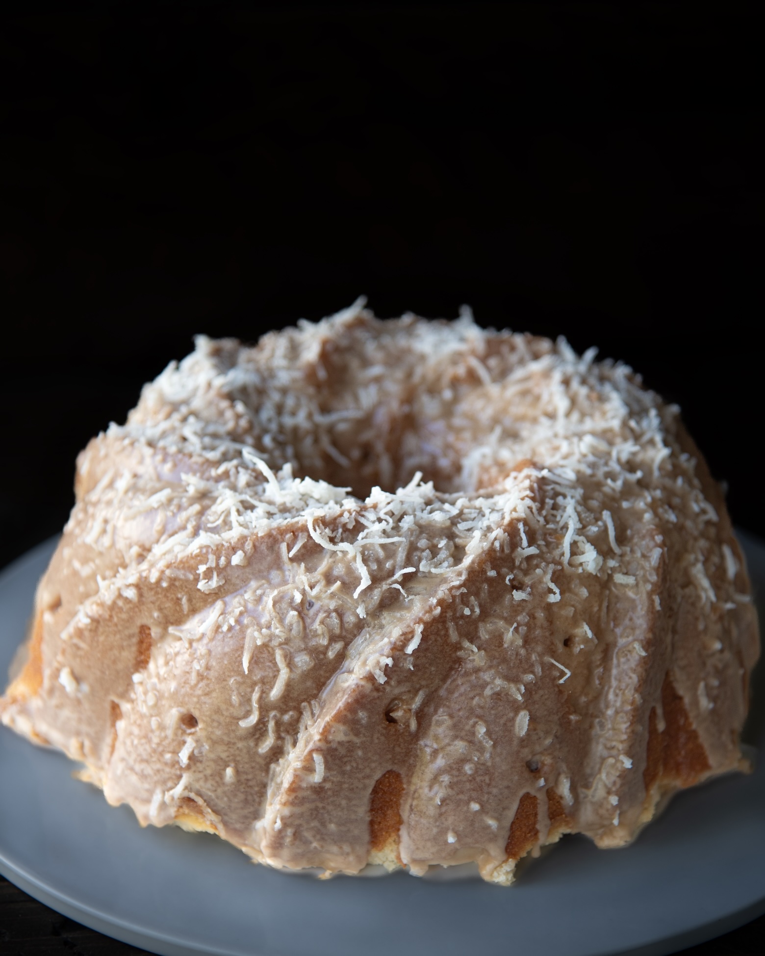 Pineapple coconut Bundt cake topped with coconut frosting and shredded coconut on a white plate.